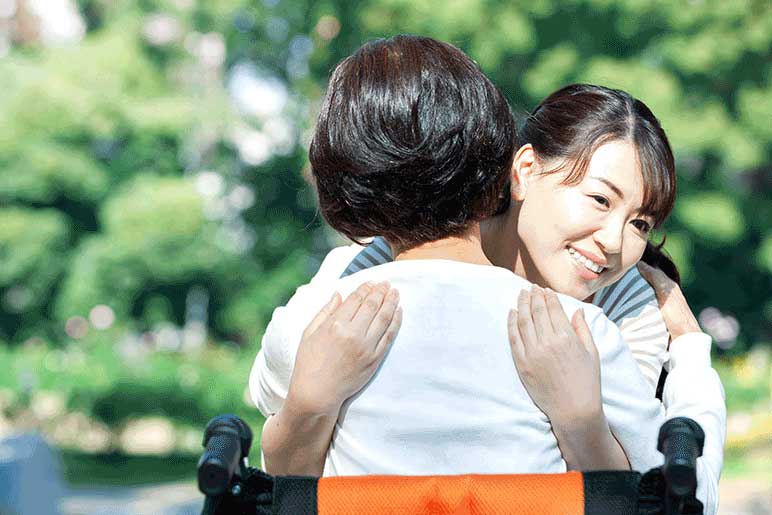 Smiling female healthcare worker hugging elderly female sitting in a wheelchair.