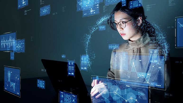 Young businesswoman sitting at desk watching hologram screens of a variety of informational charts.