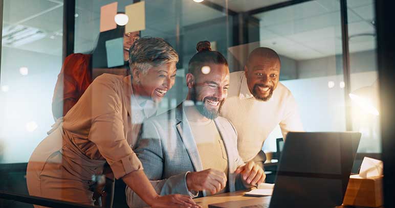 A diverse business team cheering together in their office while working on a laptop.