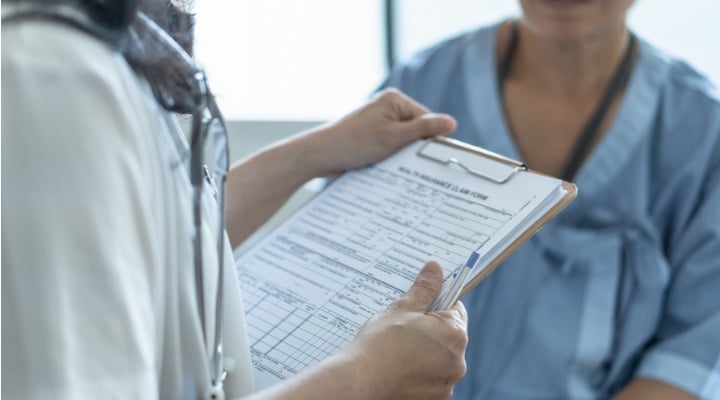 Doctor holding clipboard with health insurance claim form.