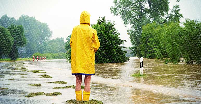 Hero image: Woman in a yellow rain jacket and yellow boots walking on a flooded street.