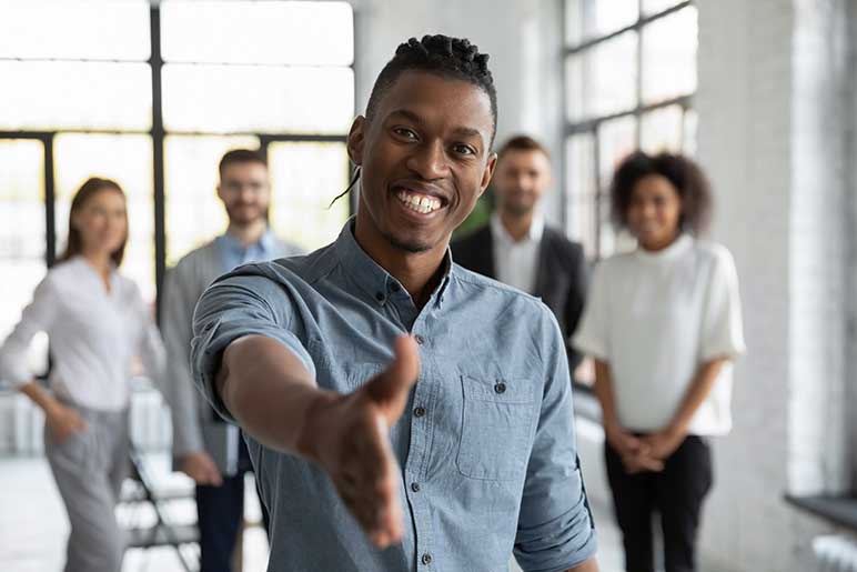 Photo of smiling young businessman reaching out his hand for a handshake; getting acquainted at workplace.