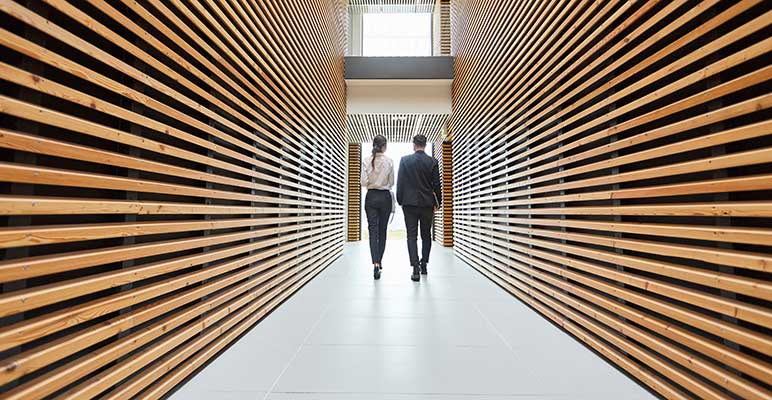 Two businesspeople are walking in a modern office corridor in one direction.
