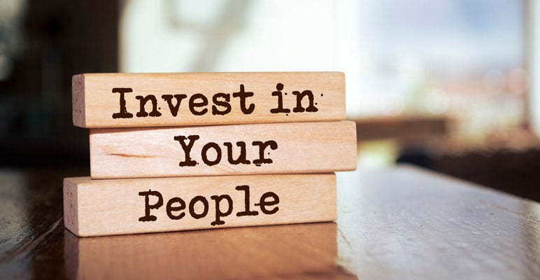 Photo of three wooden blocks stacked on top of each other with the words “Invest in Your People” written on them.