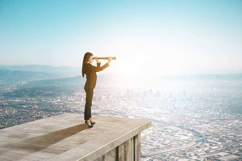 Businesswoman standing on the roof of a tall office building looking through a telescope at the cityscape below. 