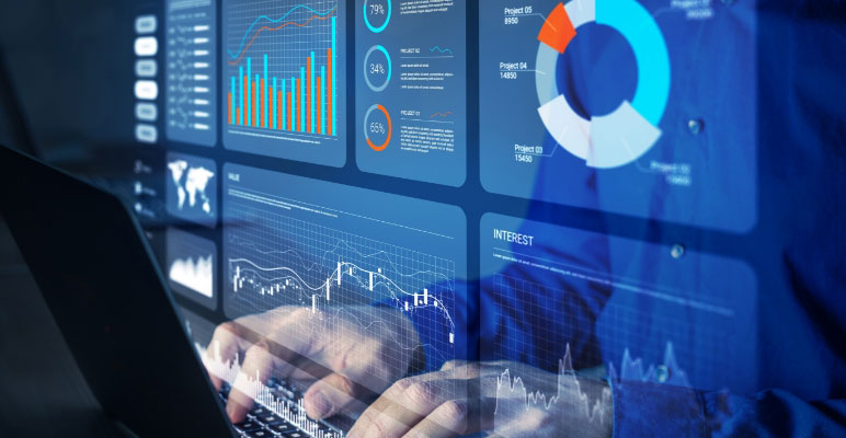 Close up photograph of male sitting at desk with the laptop screen showing bar graphs and pie charts reflecting on his shirt.